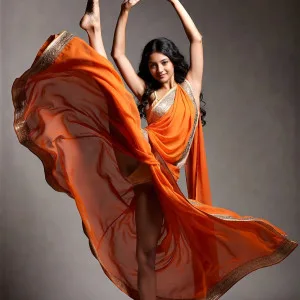 Elegant Indian woman in orange saree dancing gracefully in studio