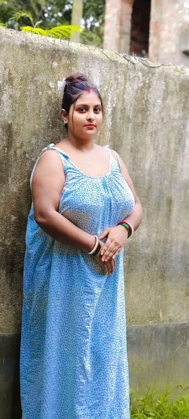 Curvy Bangali woman in blue maxi dress leaning on wall