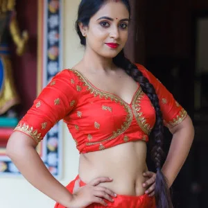 Indian woman in red traditional attire standing confidently with hands on hips